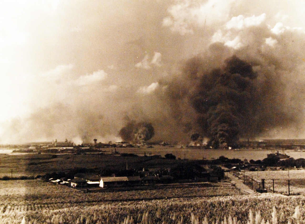 <p>80-G-32425: Pearl Harbor Attack, 7 December 1941. Panorama view of Pearl Harbor, during the Japanese raid, with anti-aircraft shell bursts overhead. The photograph looks southwesterly from the hills behind the harbor. Large column of smoke in lower right center is from the burning USS Arizona (BB-39). Smoke somewhat further to the left is from the destroyers Shaw (DD-373), Cassin (DD-372) and Downes (DD-375), in drydocks at the Pearl Harbor Navy Yard.&nbsp;</p>
