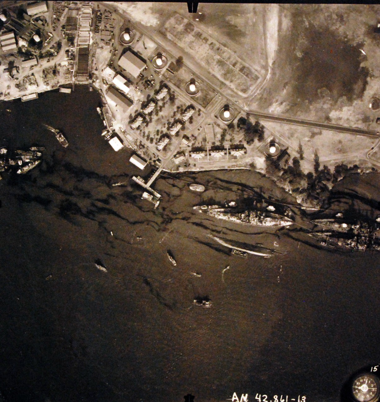 80-G-387574:  Pearl Harbor Attack, 7 December 1941.  Aerial view of "Battleship Row" moorings on the southern side of Ford Island, 10 December 1941, showing damage from the Japanese raid three days earlier.  Diagonally, from left center to lower right are: USS Maryland (BB-46), lightly damaged, with the capsized USS Oklahoma (BB-37) outboard. A barge is alongside Oklahoma, supporting rescue efforts. USS Tennessee (BB-43), lightly damaged, with the sunken USS West Virginia (BB-48) outboard. Note dark oil streaks on the harbor surface, originating from the sunken battleships. Photographed by VJ-1 at an altitude of 3,000 feet and released November 9, 1950. U.S. Navy photograph, now in the collections of the National Archives.       (9/22/2015).
