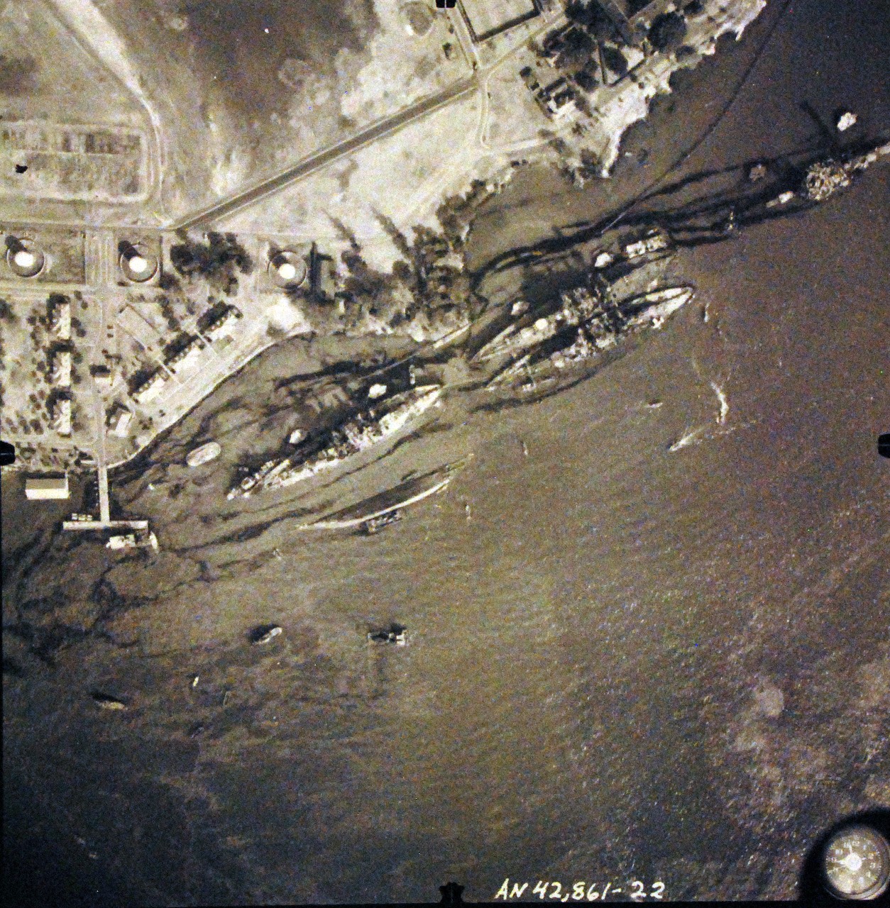 80-G-387583:  Pearl Harbor Attack, 7 December 1941.  Aerial view of "Battleship Row" moorings on the southern side of Ford Island, 10 December 1941, showing damage from the Japanese raid three days earlier.  Diagonally, from left center to lower right are: USS Maryland (BB-46), lightly damaged, with the capsized USS Oklahoma (BB-37) outboard. USS Tennessee (BB-43), lightly damaged, with the sunken USS West Virginia (BB-48) outboard. USS Arizona (BB-39), sunk, with her hull shattered by the explosion of the magazines below the two forward turrets. Note dark oil streaks on the harbor surface, originating from the sunken battleships. Photographed by VJ-1 at an altitude of 3,000 feet and released November 9, 1950. U.S. Navy photograph, now in the collections of the National Archives.      (9/22/2015).