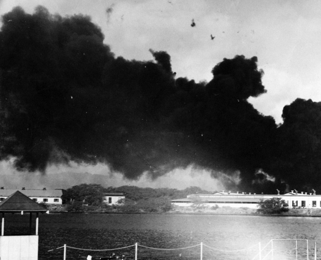 80-G-32731:   Japanese Attack on Pearl Harbor, December 7, 1941.   Oil flames resulting from the attack.  This view looks toward Magazine Island from the Submarine Base.  Note the enemy plane in dive bomb attack as fire burns nearby. Official U.S. Navy photograph, now in the collections of the National Archives.           (9/9/2015).