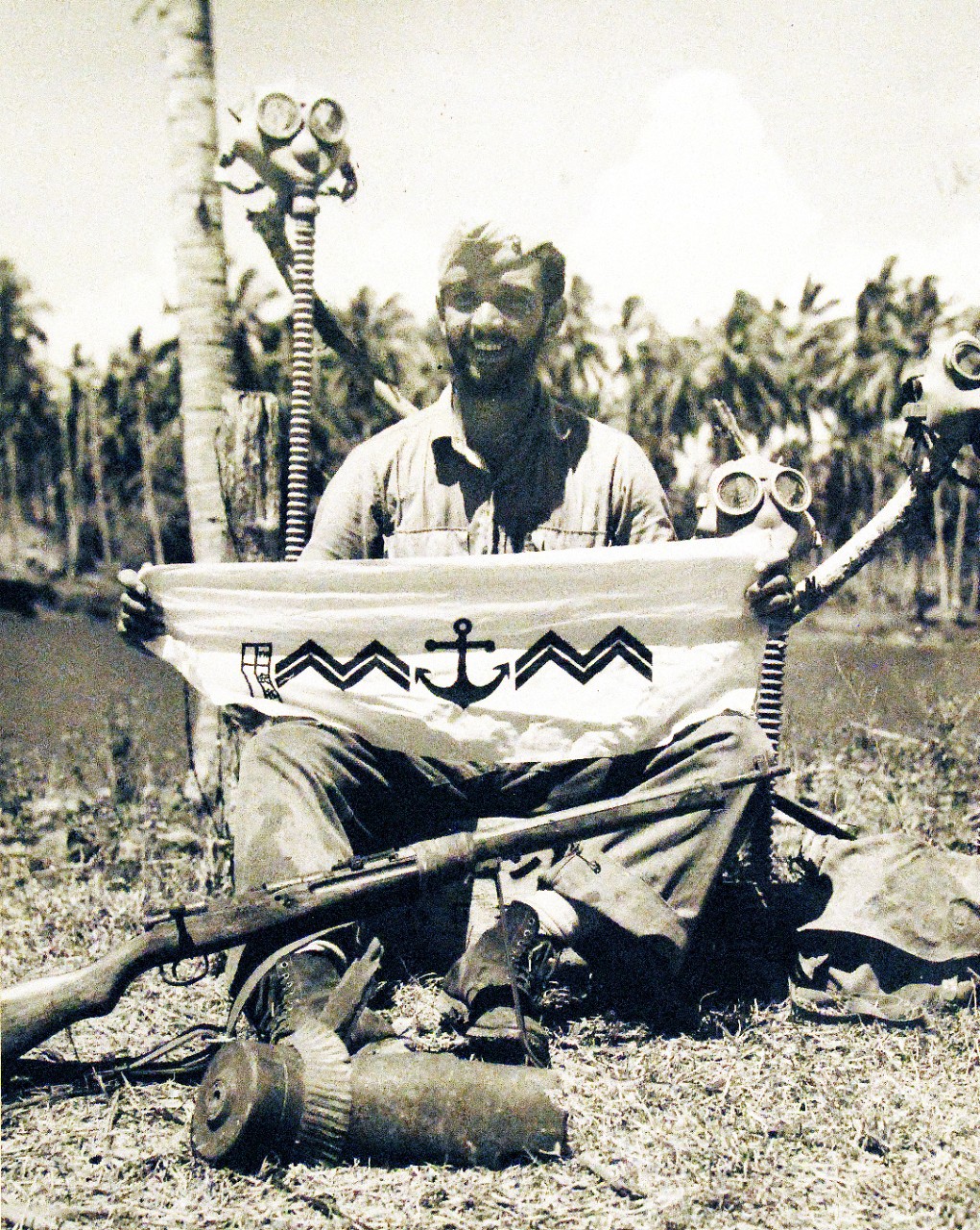 80-G-40285:  Guadalcanal Operation, August 1942-February 1943  U.S. Marine private Frank Massaro at Guadalcanal Island displays (as per original caption – “Japanese marine emblem.”)  Behind him are Japanese gas masks, 1942. U.S. Navy Photograph, now in the collections of the National Archives  (2015/10/20).