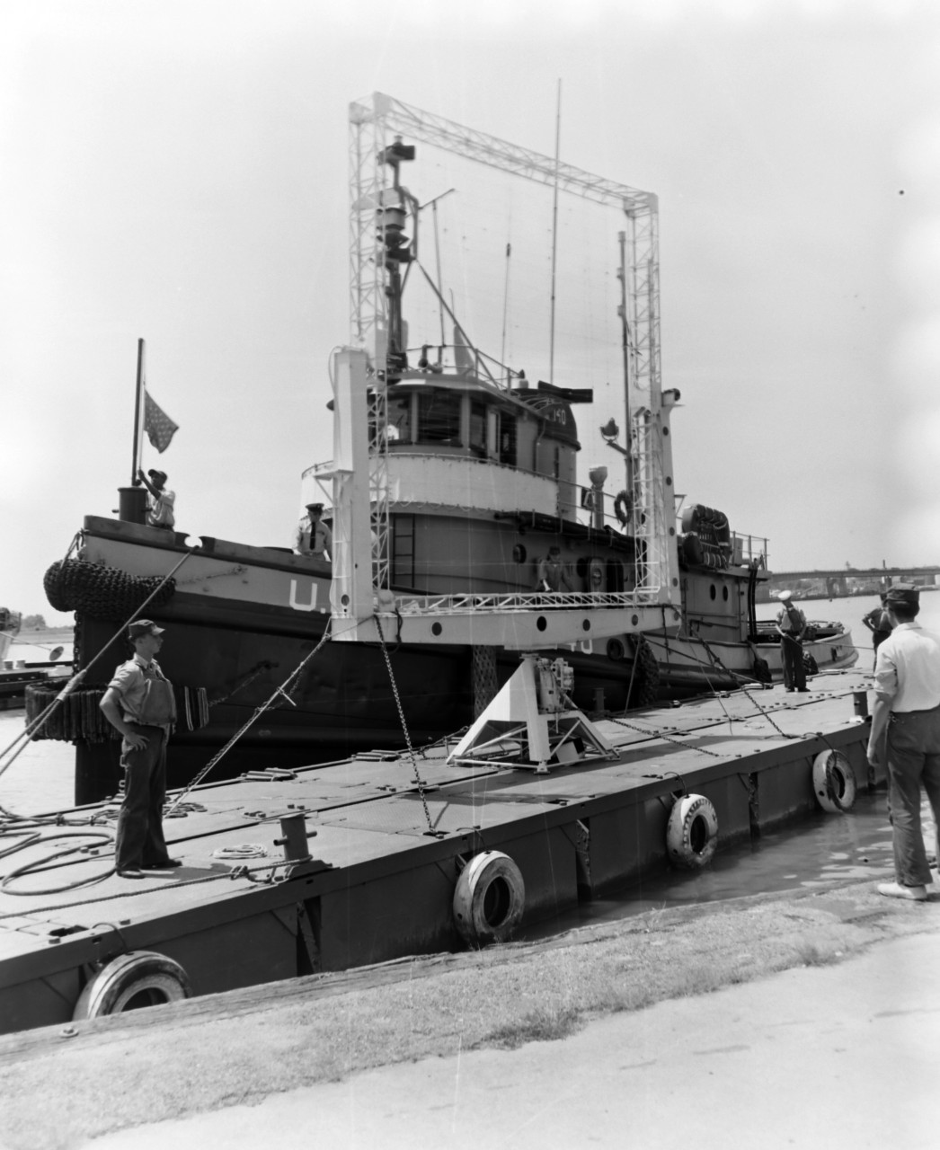 NMUSN-1017:   XAF Radar Antenna, 1960s.   Being delivered to the Washington Navy Yard for display.  Note the U.S. Navy tug alongside a small thin barge carrying the radar antenna.  The tug appears to be USS Wahtah (YTB-140).  This radar was the first shipboard radar to be installed onboard a U.S. Navy ship, USS New York (BB-34).  Surviving World War II, it was brought to the Washington Navy Yard where it was on exterior display until the mid-1980s where it was placed into storage.   Following conservation, the radar is now on display at the National Electronics Museum, Linthicum, Maryland.    Original is a black and white negative.   National Museum of the U.S. Navy Photograph Collection.