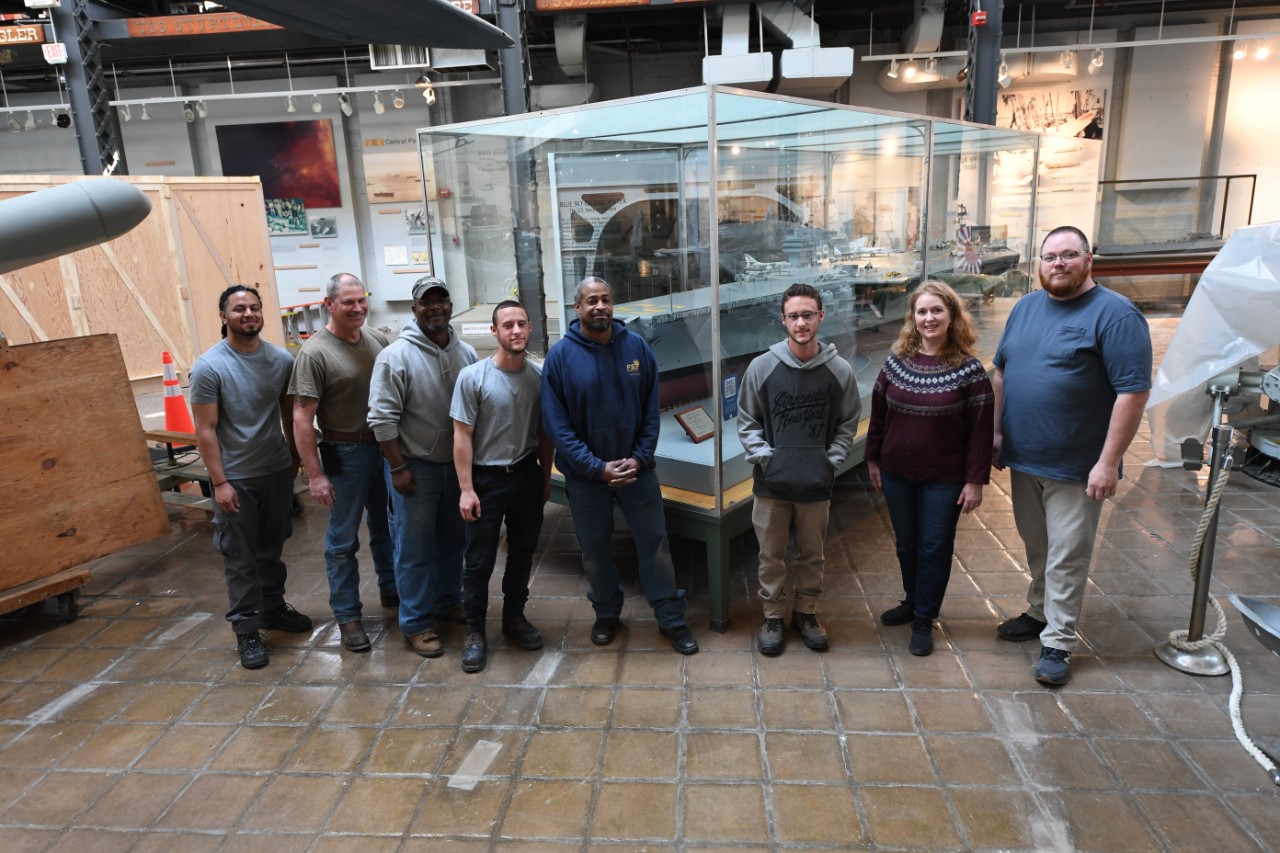 230410-N-BK765-0368: Naval Surface Warfare Center, Carderock Division’s model moving team poses in front of the USS Forrestal (CVA 59) model at its new home in the National Museum of the U.S. Navy at the Washington Navy Yard in Washington, D.C., ...