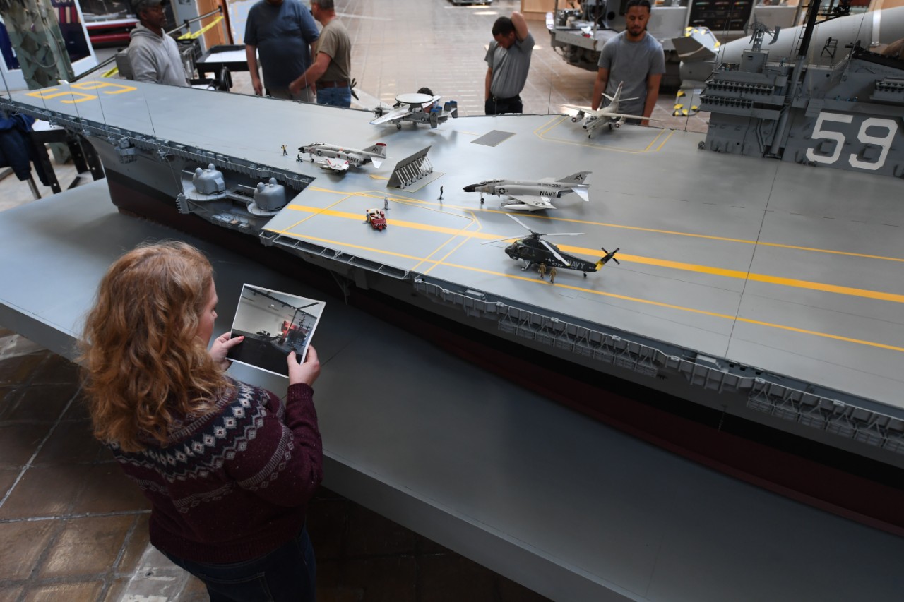 230410-N-BK765-0434: Naval Surface Warfare Center, Carderock Division’s Jennifer Marland, the Assistant Curator with the Office of the Curator, carefully examines a photograph to ensure all parts and pieces of the USS Forrestal model are put back...