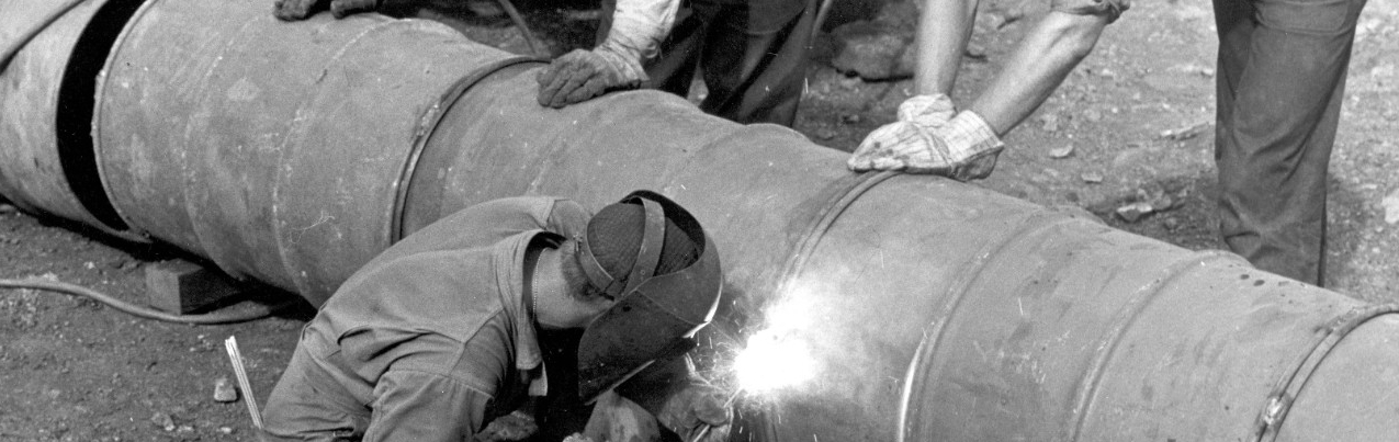 Three Seabees welding 55-gallon drums together for a sewage pipeline
