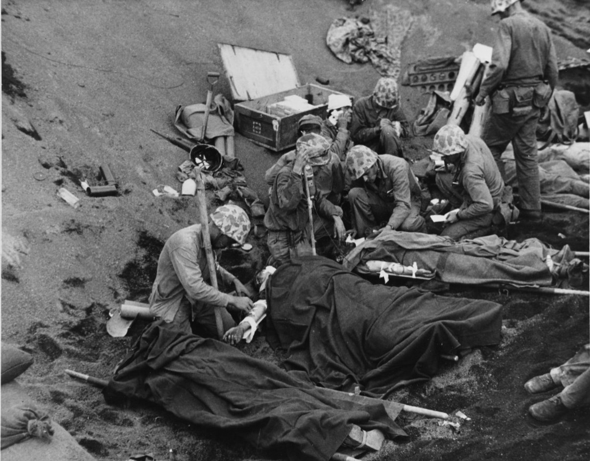 Iwo Jima Operation, 1945 U.S. Navy doctors and corpsmen administer to wounded Marines at an Iwo Jima first aid station, 20 February 1945. Navy Chaplain Lieutenant (Junior Grade) John H. Galbreath (right center) is kneeling beside a man who has se...