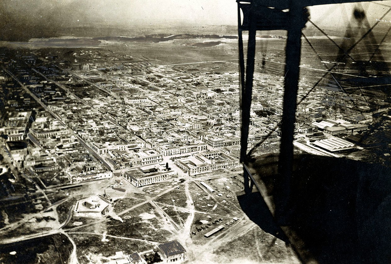 Aerial view of city with a biplane wing visible in foreground.