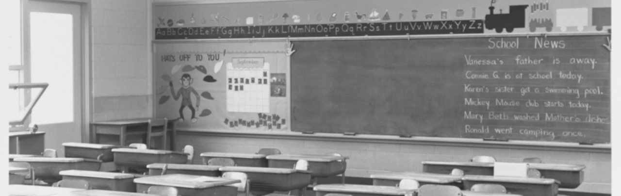 Black and white photo of an empty elementary school classroom typical of the early 1960s.
