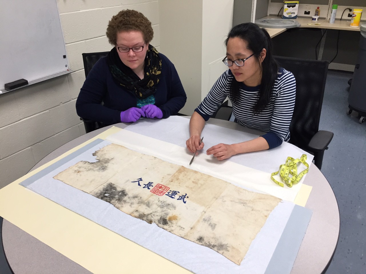 Two conservators examine a Japanese prayer towel.