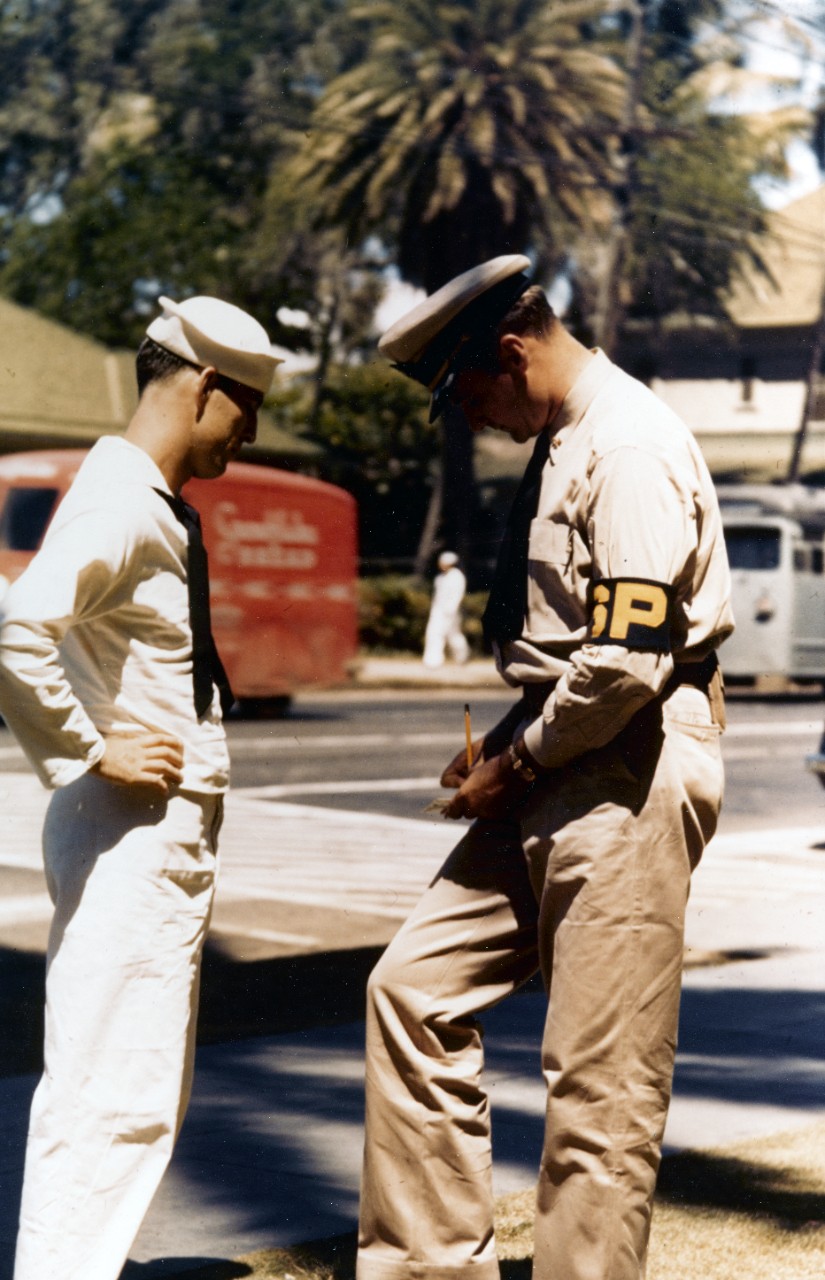 Shore patrolman writes a ticket for a sailor caught "off guard" in Hawaii, during World War II.