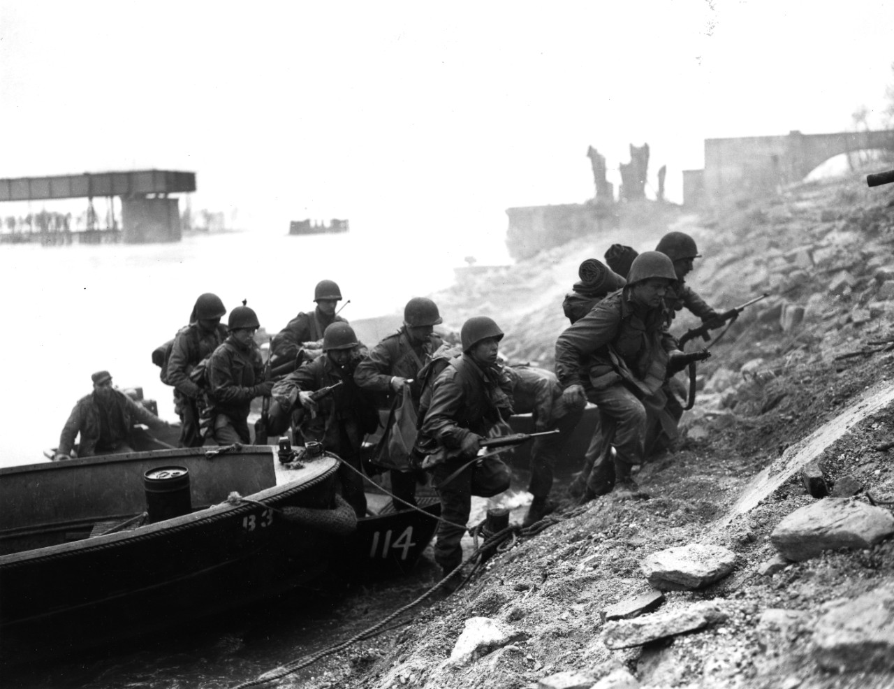 Soldiers of the US Army 7th Infantry Regiment, 3rd Division, leave the assault boat that took them across the Rhine River, 26 March 1945. They climb the river's bank, next to a destroyed bridge in the Frankenthal area. Most of these men are armed with M-1 carbines.