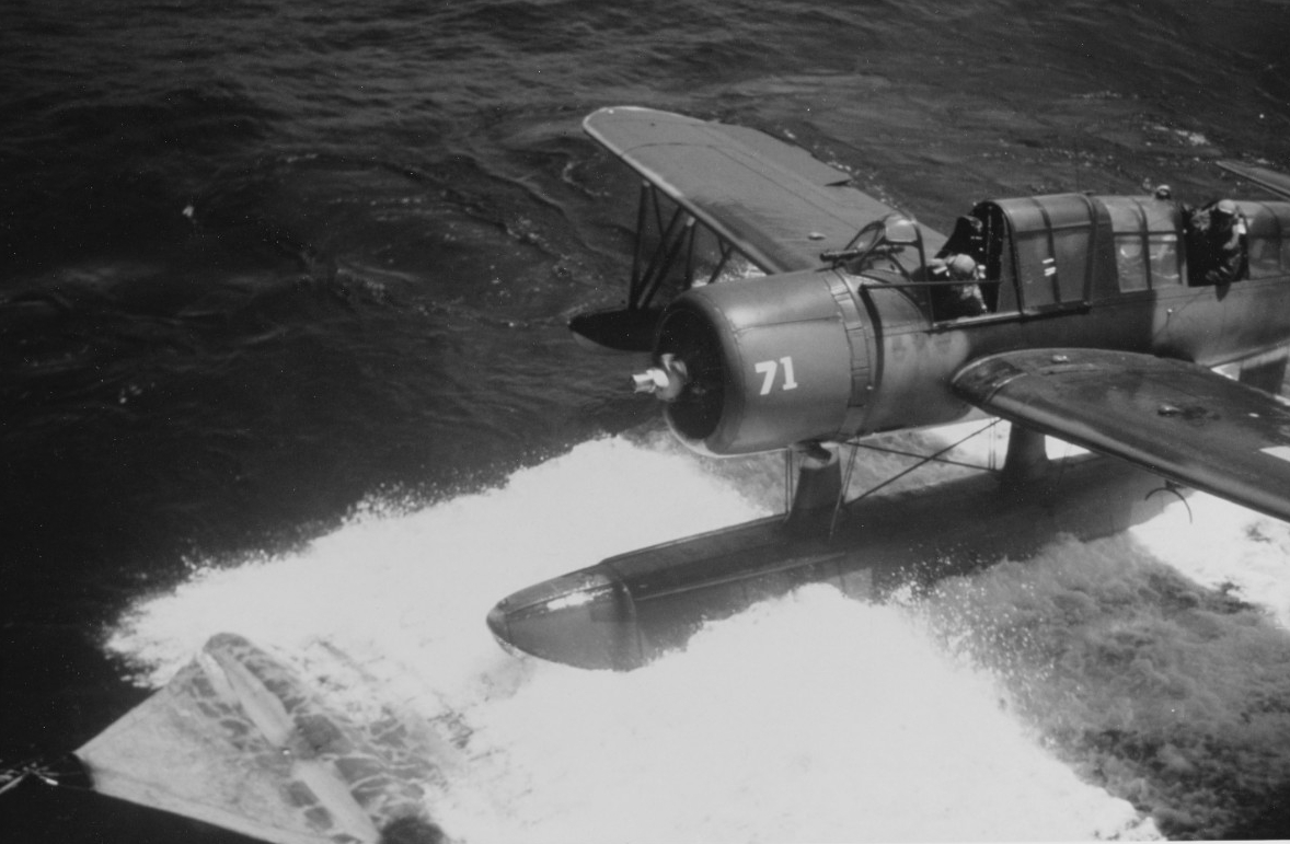 Photo 80-G-K-1954: Vought OS2U "Kingfisher"floatplane taxis up on the recovery mat of USS Quincy (CA-71), circa 1944. Note pilot leaning out of the cockpit.