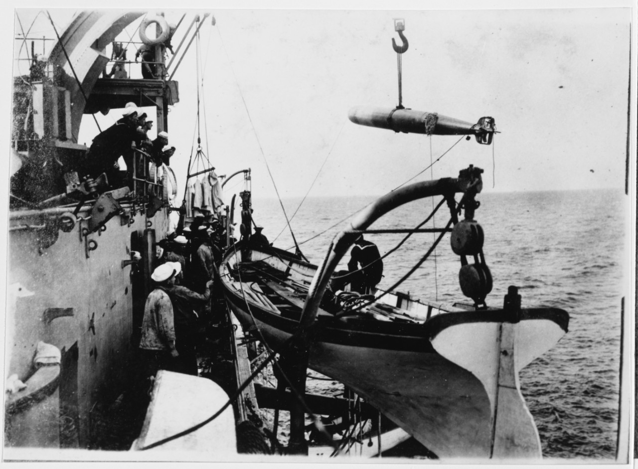 USS MAINE (BB-10) Hoisting in a 18-inch torpedo, after practice, circa 1904-1905. Note cutter in foreground.