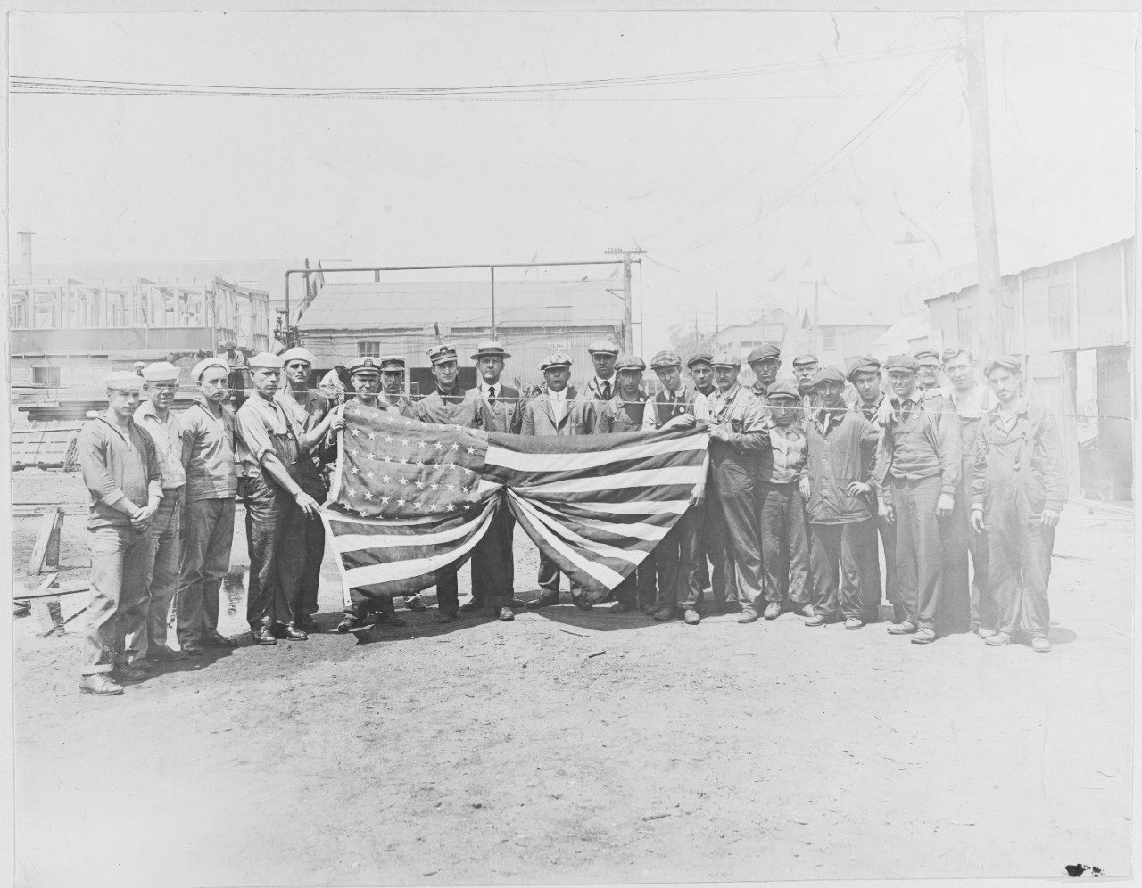Employees of Lake Torpedo Boat Company pose for portrait holding large American Flag