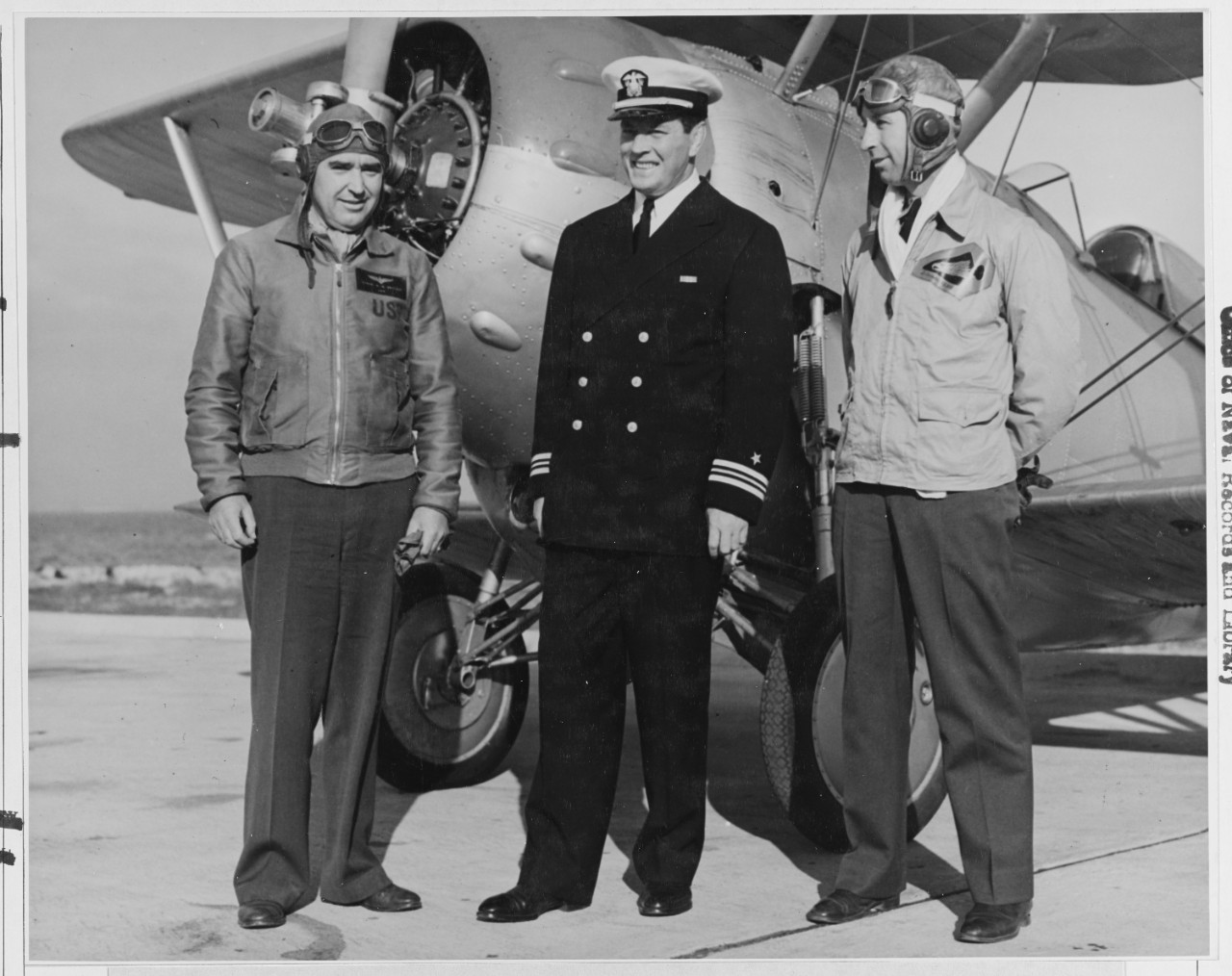 Comdr. W. G. Switzer, (left) Officer in charge, Aviation Cadet Regiment at the Naval Air Station Pensacola, Florida and Lt. Comdr D.D. Wilcox, (center) officer -in charge, Cadet regiment at the New Naval Air Station, Corpus Christi Texas, explains the finer points of flying to Lt. Comdr. J.J. (Gene) Tunney the Navy's new athletic director, at the Naval  Air Station, Pensacola, Fla.