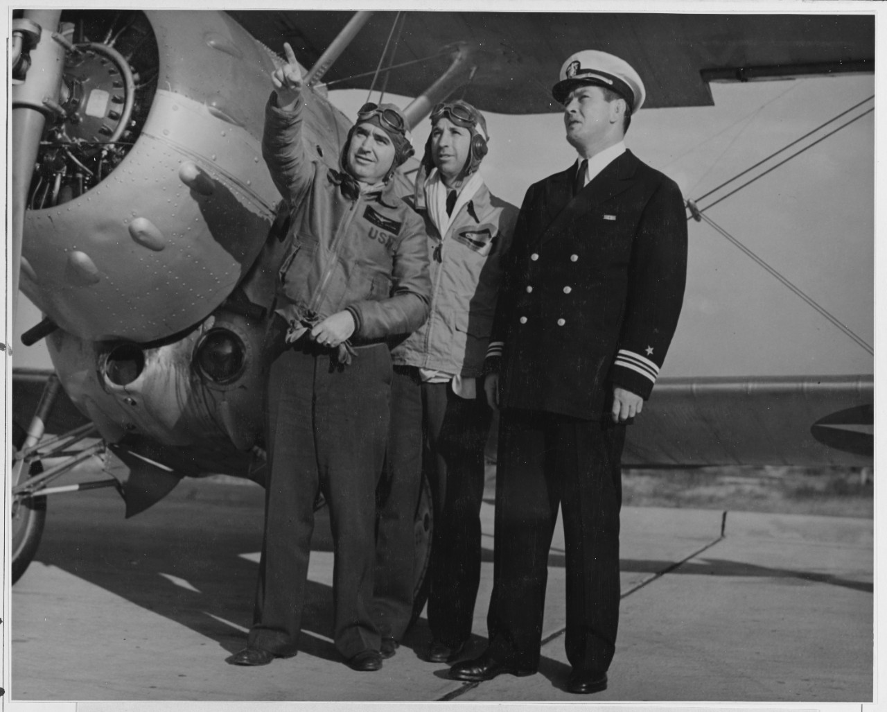 Comdr. W. G. Switzer, (left) Officer in charge, Aviation Cadet Regiment at the Naval Air Station Pensacola, Florida and Lt. Comdr D.D. Wilcox, (center) officer -in charge, Cadet regiment at the New Naval Air Station, Corpus Christi Texas, explains the finer points of flying to Lt. Comdr. J.J. (Gene) Tunney the Navy's new athletic director, at the Naval  Air Station, Pensacola, Fla.