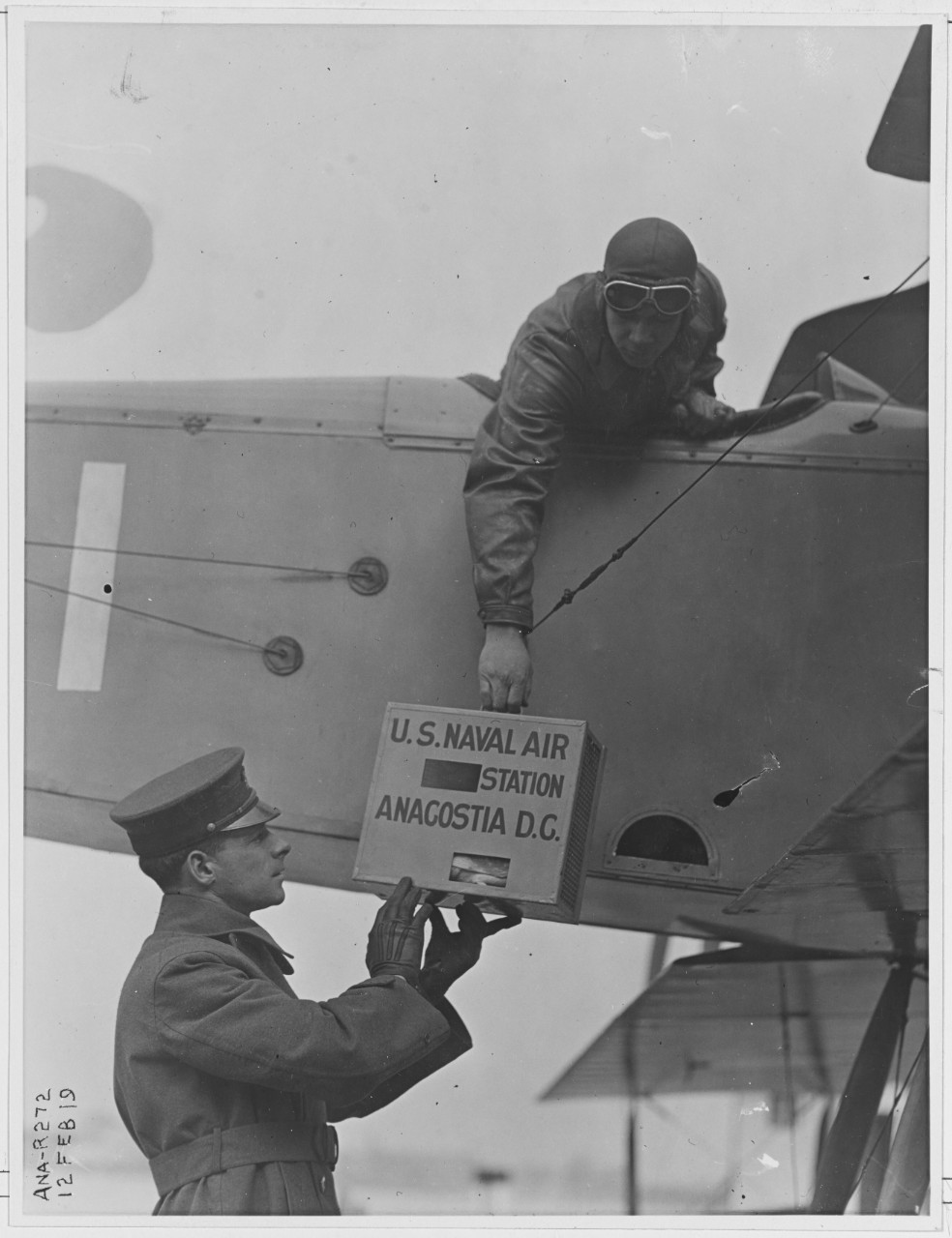 Four-bird size pigeon box containing pigeons is handed to the pilot in airplane. February 12, 1919