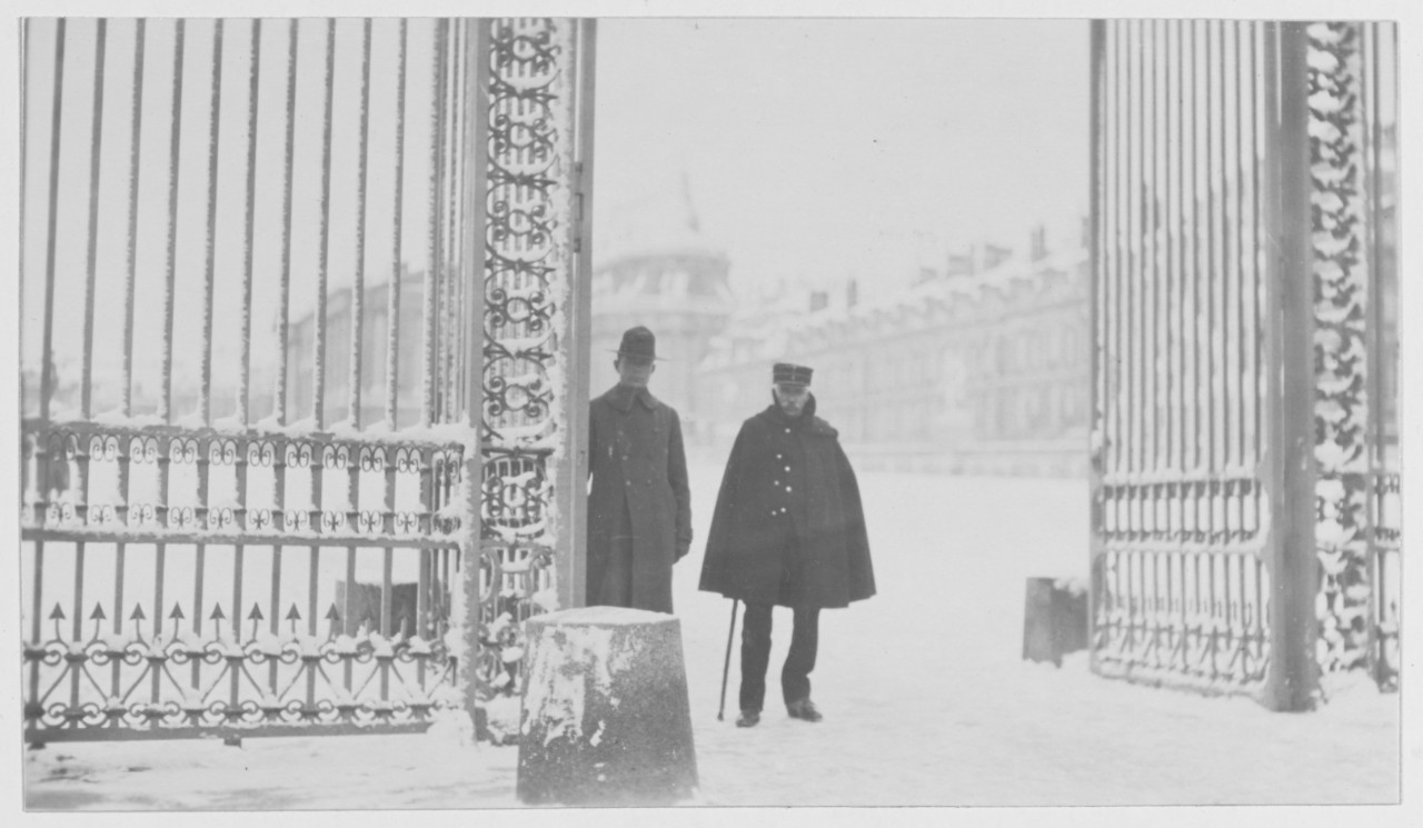Two men stand at the gate to Versailles in snowy winter scene during World War I, Versailles, France