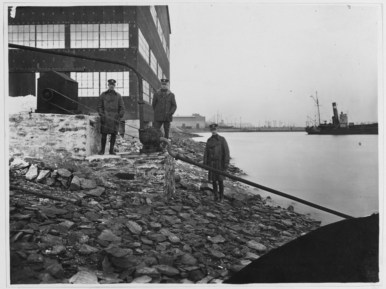 Men stand near coastline, next to a Pump for handling of sea water for the condensing and scrubbing of Hydrogen gas. Brest, France, 1917 - 1919
