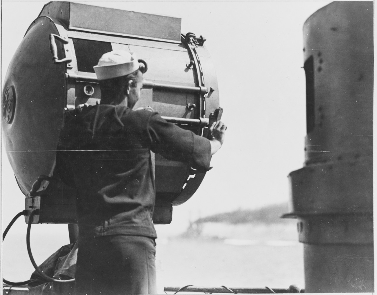 Sailor stands next to searchlight on battleship