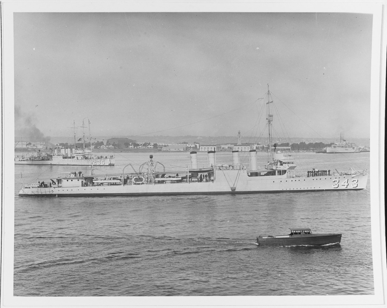 Clemson-class destroyer USS Noa (DD-343) underway in San Diego Harbor, about 1930. Note yacht underway in the foreground, and USS Kane (DD-235) moored alongside another destroyer in the background. Other vessels can be seen in the distant background, as well as a far-off airship hangar.