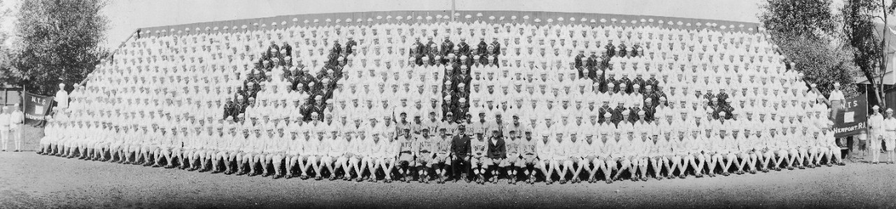 Enlisted men on bleachers at Naval Training Station Newport, RI, 1923. Enlisted are mainly in white, with those in blue spelling out "NTS". Note the station's baseball team in the center.