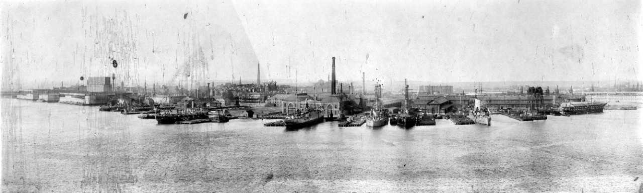 Panoramic photo of the Boston Navy Yard, 1913. View shows the entire expanse of the navy yard, as seen from across the river. Ships seen include: USS  Virginia (BB-13), USS Rhode Island (BB-17), & an armored cruiser - either USS North Carolina (CA-12) or USS Montana (CA-13). Photo has water damage along left side. 