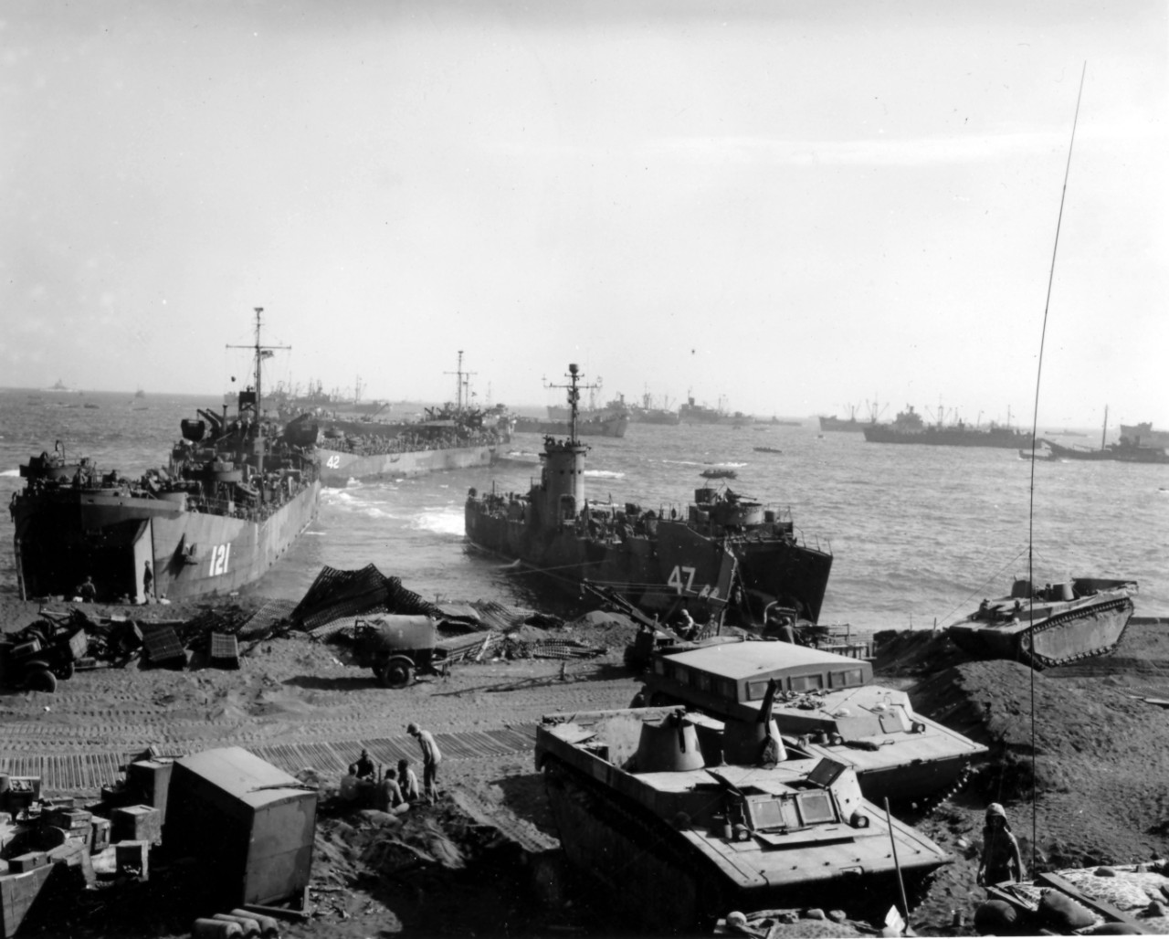 <p>Personnel, supplies, and various LVTs remain on the beach at Iwo Jima on 25 February 1945. <a href="https://www.history.navy.mil/content/history/nhhc/research/histories/ship-histories/danfs/l/lst-121.html"><i>LST-121</i></a> and <i>LSM-47</i> are beached at the shoreline, while <a href="https://www.history.navy.mil/content/history/nhhc/research/histories/ship-histories/danfs/l/lst-42.html"><i>LST-42</i></a> maneuvers behind them. Image is from the Admiral Harry W. Hill Collection.</p>
