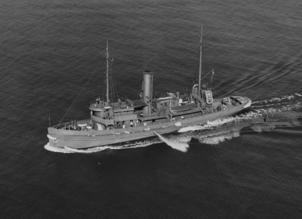 Aerial view of Acushnet underway in Hampton Roads, 7 October 1944, soon after the completion of repairs for damage suffered in a hurricane the previous month. She is apparently testing one of her fire hoses. Note shadow of the plane from which th...