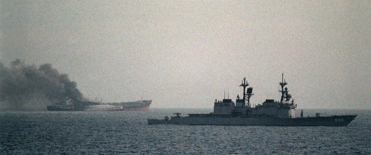 Chandler passes by the burning Greek tanker Ariande as fire tugs attempt to put out the blaze on 15 December 1987. Ariande had been attacked by small gunboats. Just three days prior, Chandler rescued crewmembers of the Cypriot tanker Pivot which ...