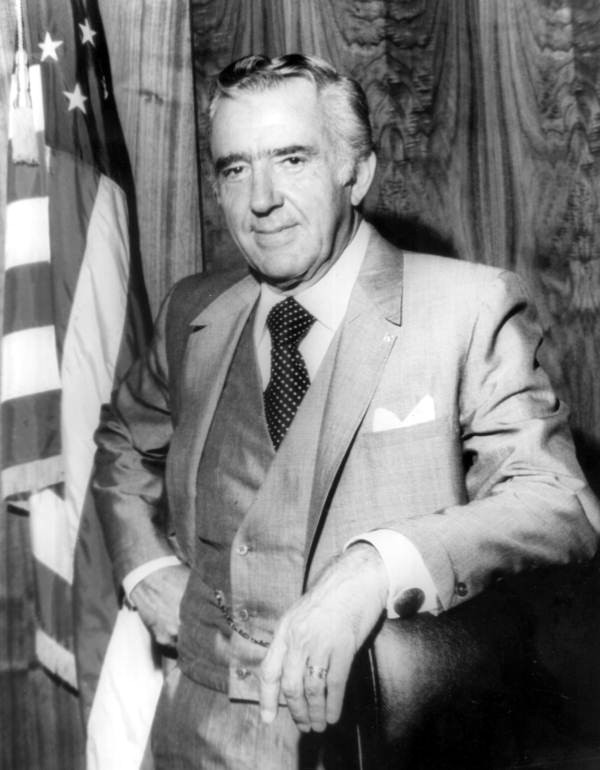 Portrait of Philip Frederic Ashler, an older Caucasian male in a suit and tie, with American flag in left of photo.